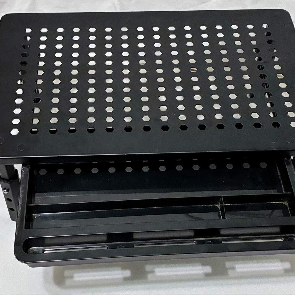 Adjustable height black perforated metal monitor stand with a pull-out drawer. 